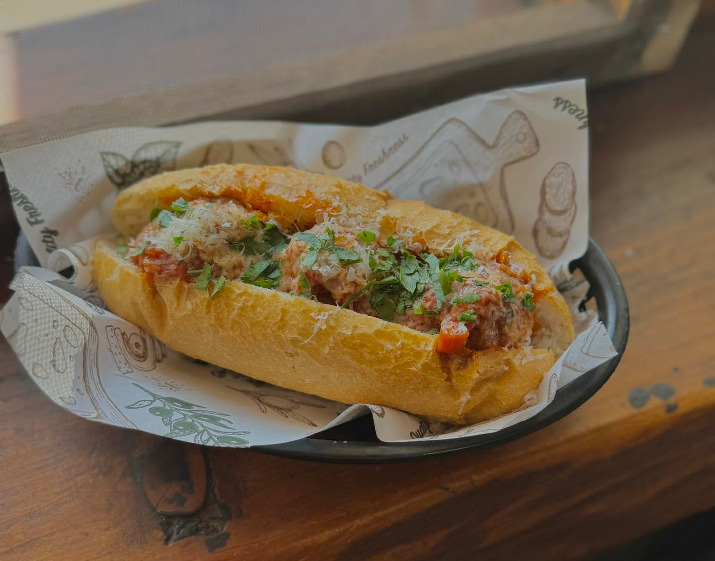 Loaded meatball sub sandwich topped with fresh herbs and grated cheese in a toasted roll