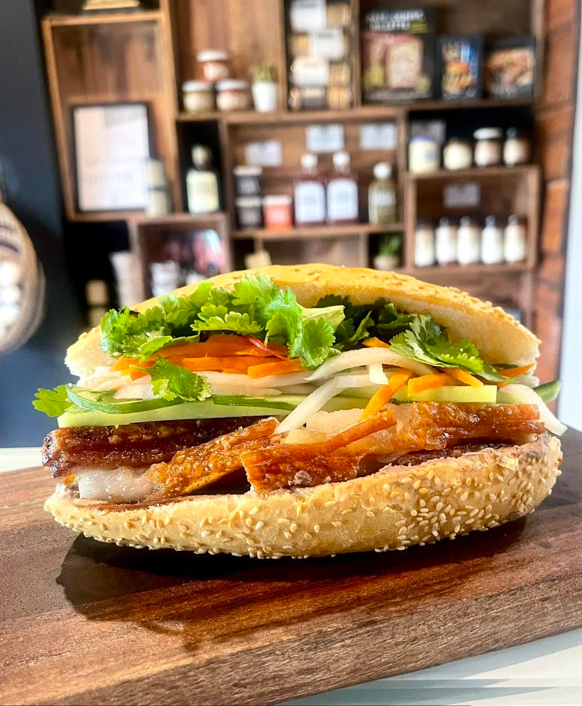 Crispy pork belly banh mi with fresh cilantro, pickled vegetables, and cucumber on a sesame seed roll