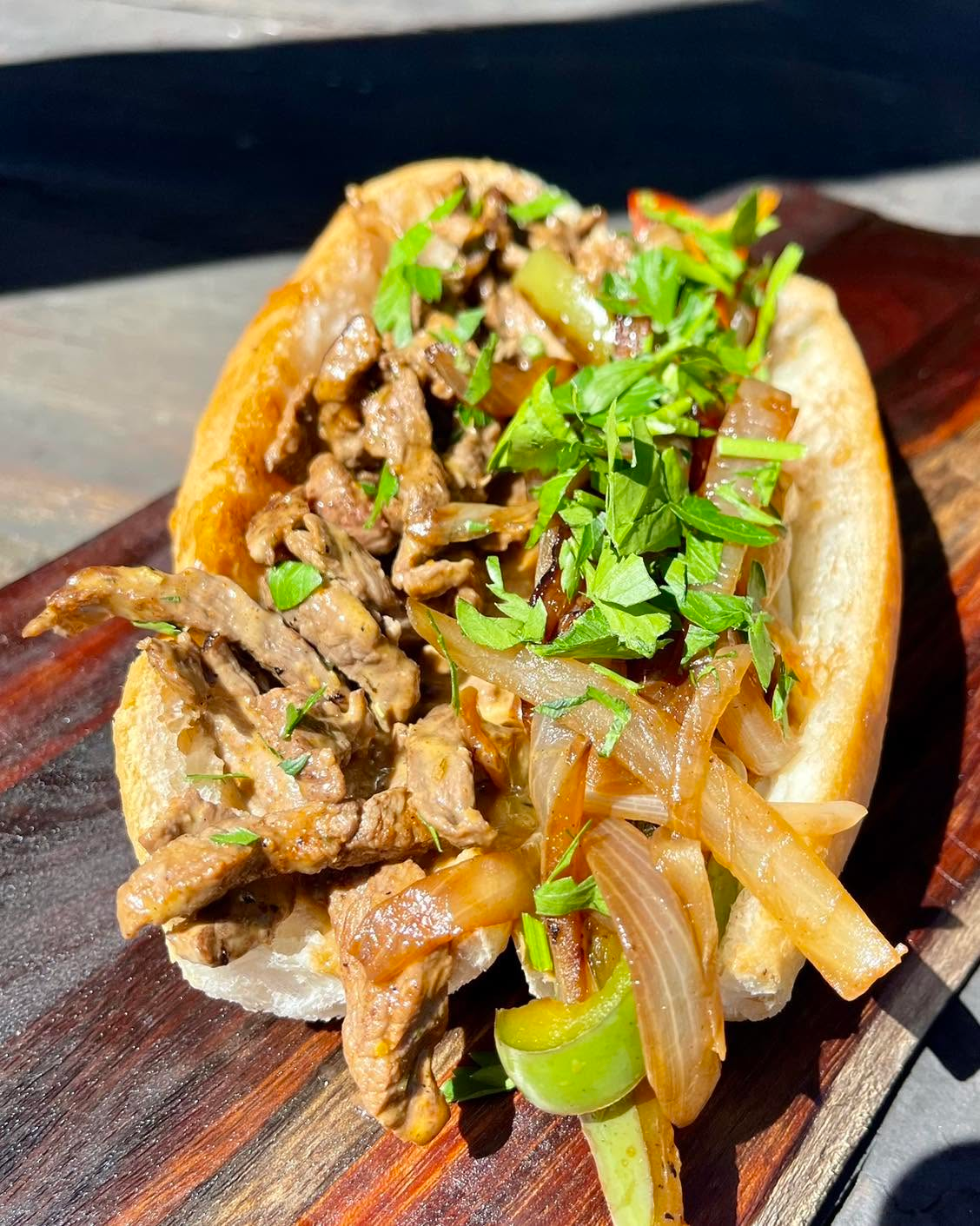 Loaded beef sub with caramelised onions, fresh herbs, and green onions on a toasted roll